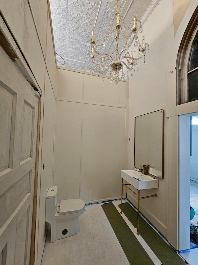 bathroom with a sink, toilet, a chandelier, and wood finished floors