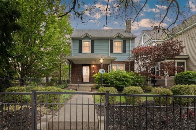 traditional-style home with a fenced front yard, brick siding, a chimney, and a gate