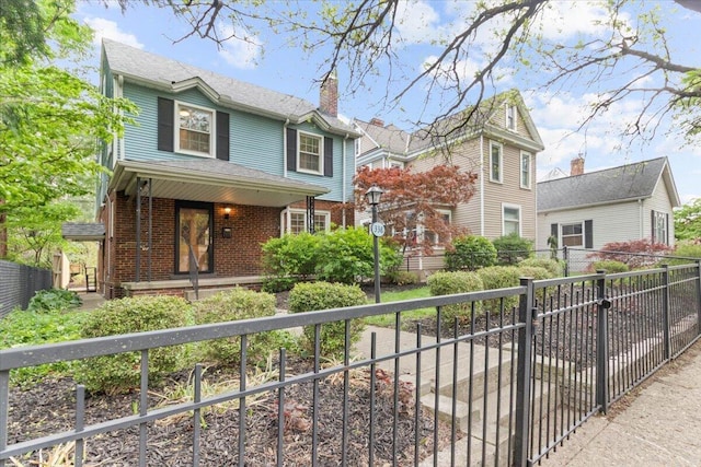 traditional-style house featuring covered porch, brick siding, fence, and a chimney