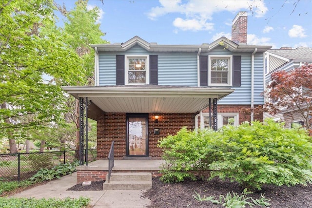 view of front of property featuring brick siding, fence, a chimney, and a porch