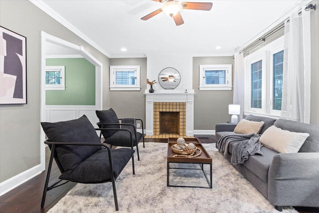 living room featuring a ceiling fan, baseboards, wood finished floors, a tile fireplace, and ornamental molding