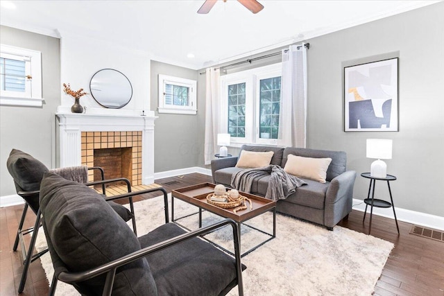 living area with visible vents, ornamental molding, wood finished floors, baseboards, and a ceiling fan