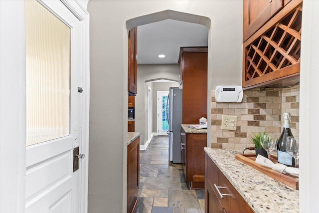 kitchen with stone tile flooring, arched walkways, light stone counters, and freestanding refrigerator