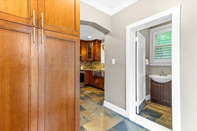 bathroom featuring crown molding, vanity, baseboards, stone finish flooring, and tasteful backsplash