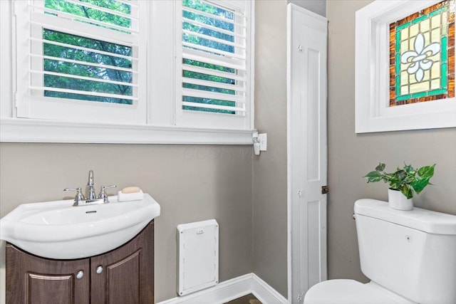 half bathroom with vanity, baseboards, and toilet