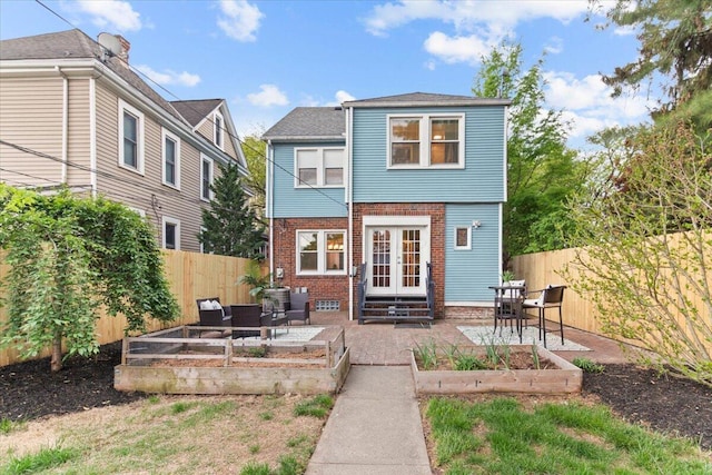 back of property featuring french doors, a fenced backyard, and a garden