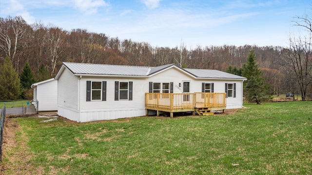 view of front facade with metal roof, fence, a wooden deck, a front yard, and a forest view