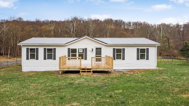 view of front of property with a view of trees, a front lawn, a deck, and metal roof