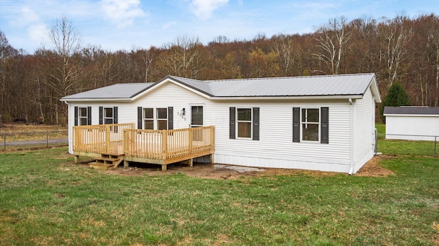 rear view of property with fence, metal roof, a forest view, a deck, and a lawn