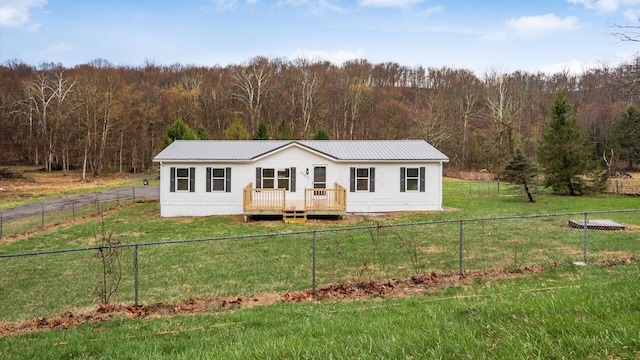view of front of house with metal roof, a wooded view, a deck, and a front yard