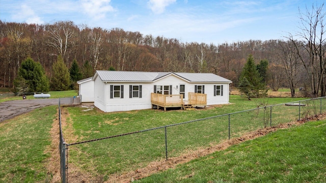 view of front of home featuring a view of trees, a deck, a front lawn, metal roof, and fence private yard