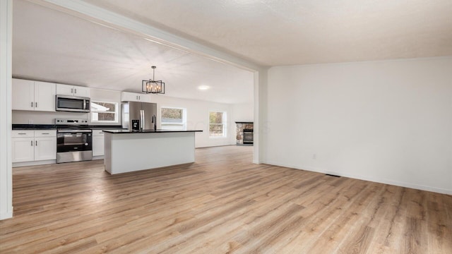 kitchen featuring white cabinets, stainless steel appliances, dark countertops, open floor plan, and an inviting chandelier