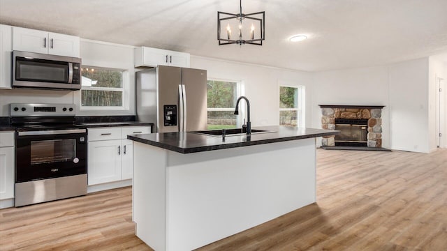 kitchen with a sink, light wood-style flooring, stainless steel appliances, dark countertops, and white cabinets