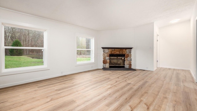 unfurnished living room featuring a stone fireplace, baseboards, and light wood-type flooring