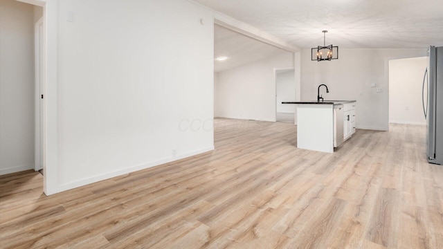 kitchen with a notable chandelier, freestanding refrigerator, light wood finished floors, vaulted ceiling with beams, and dark countertops