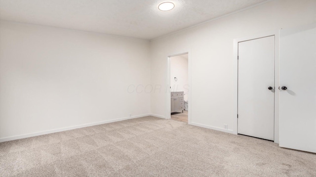 unfurnished bedroom featuring light carpet, connected bathroom, baseboards, and a textured ceiling