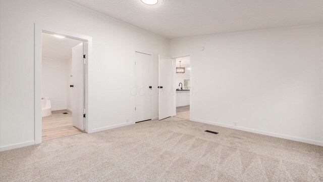 unfurnished bedroom with connected bathroom, crown molding, light colored carpet, and visible vents