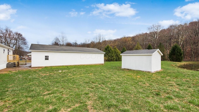 view of yard featuring a view of trees, a storage shed, and an outdoor structure