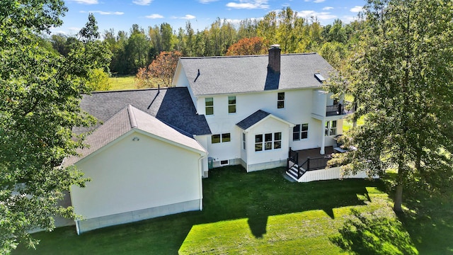 rear view of house featuring a balcony, a chimney, a lawn, and roof with shingles
