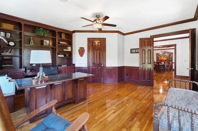 home office with a wainscoted wall, light wood-style flooring, ceiling fan, and ornamental molding