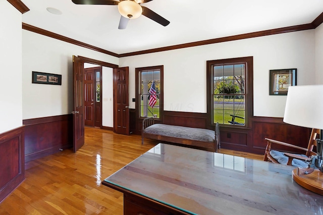 interior space featuring a ceiling fan, light wood finished floors, and wainscoting