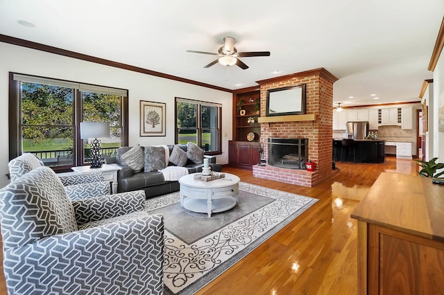 living area with a fireplace, wood finished floors, built in features, ceiling fan, and ornamental molding