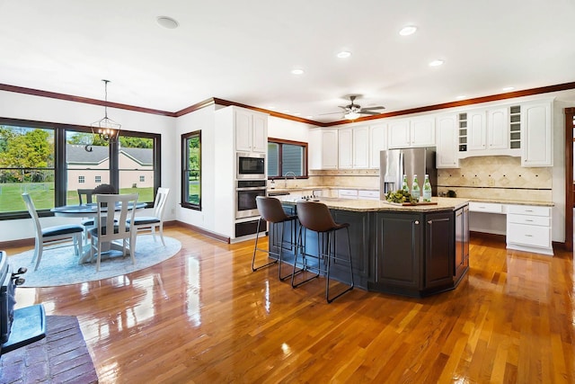 kitchen with white cabinetry, appliances with stainless steel finishes, a center island, ceiling fan, and ornamental molding