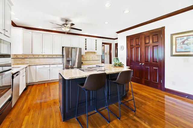 kitchen featuring crown molding, stainless steel appliances, a ceiling fan, white cabinetry, and a center island