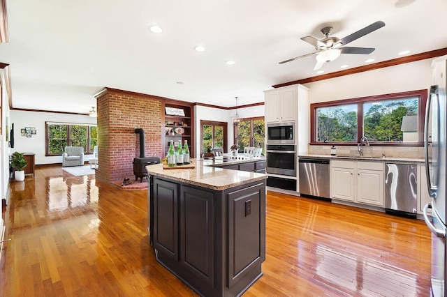 kitchen featuring ceiling fan, stainless steel appliances, white cabinetry, a sink, and a wood stove