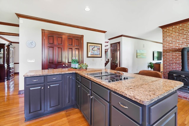 kitchen with crown molding, a wood stove, stovetop with downdraft, light stone counters, and light wood-style floors