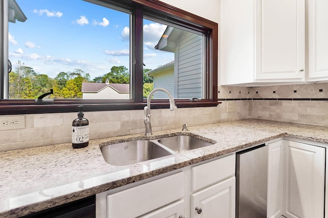 kitchen with white cabinets, a sink, light stone counters, and tasteful backsplash