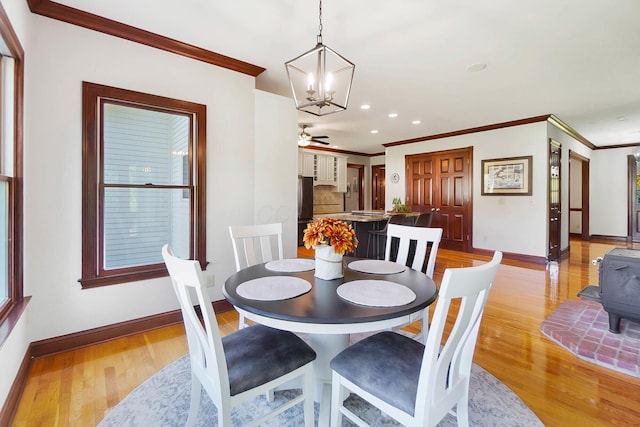 dining area featuring crown molding, a wood stove, ceiling fan with notable chandelier, light wood-type flooring, and baseboards