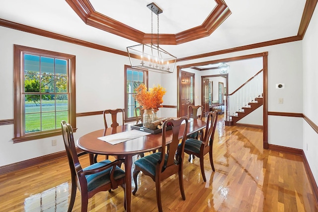 dining space with ornamental molding, baseboards, a raised ceiling, light wood-style floors, and visible vents