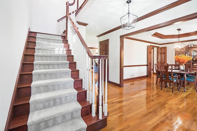 staircase with baseboards, wood finished floors, ornamental molding, and an inviting chandelier
