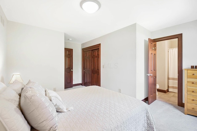 bedroom featuring a closet, ensuite bath, light tile patterned floors, and light carpet