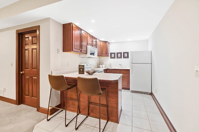 kitchen with white appliances, a breakfast bar area, baseboards, and a peninsula