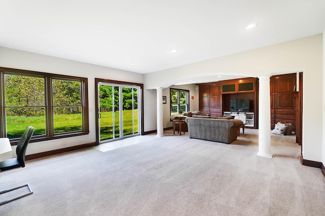 unfurnished living room featuring light colored carpet, recessed lighting, ornate columns, baseboards, and arched walkways