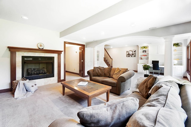 living area featuring ornate columns, arched walkways, a tile fireplace, and light carpet