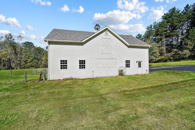 view of side of home featuring fence, an outdoor structure, a barn, and a yard