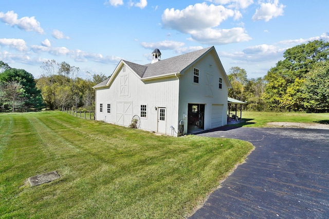 view of property exterior featuring fence, a barn, aphalt driveway, a shingled roof, and a lawn