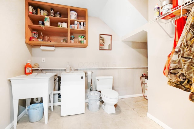 bathroom with a wainscoted wall, toilet, and lofted ceiling