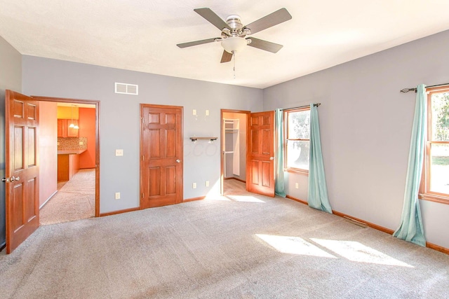 unfurnished bedroom featuring a walk in closet, carpet flooring, baseboards, visible vents, and a ceiling fan