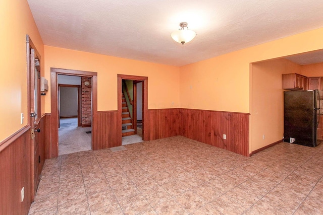 spare room featuring a wainscoted wall, wood walls, stairway, and a textured ceiling