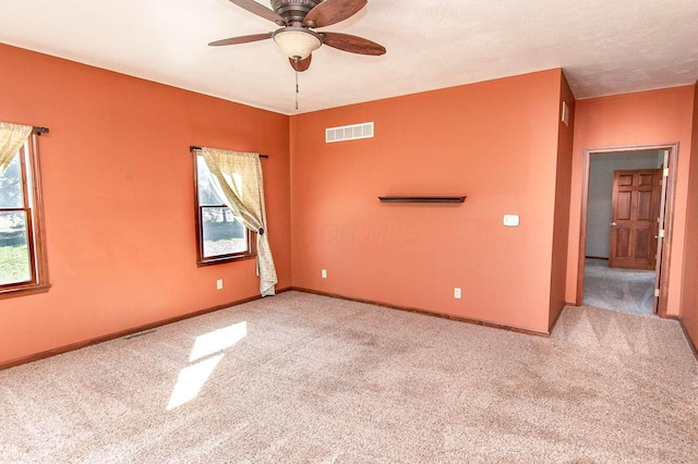 carpeted empty room with baseboards, visible vents, and a ceiling fan