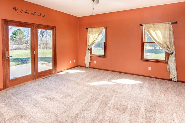 unfurnished room with carpet flooring, ceiling fan, visible vents, and a healthy amount of sunlight