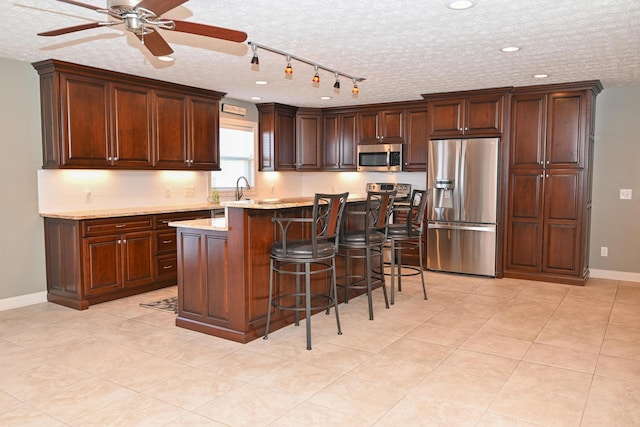 kitchen featuring a ceiling fan, a breakfast bar area, a textured ceiling, a center island, and stainless steel appliances
