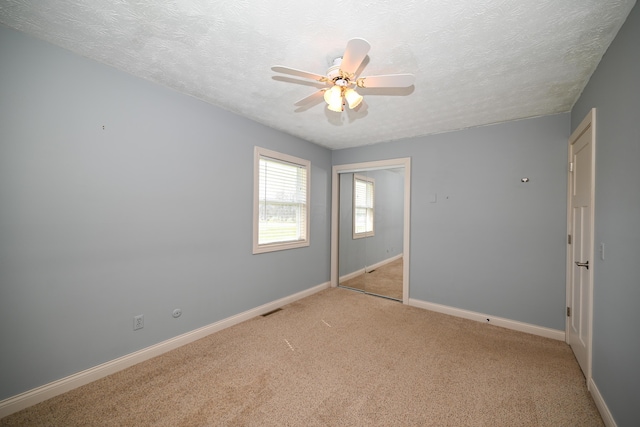 spare room with a ceiling fan, baseboards, light colored carpet, and a textured ceiling