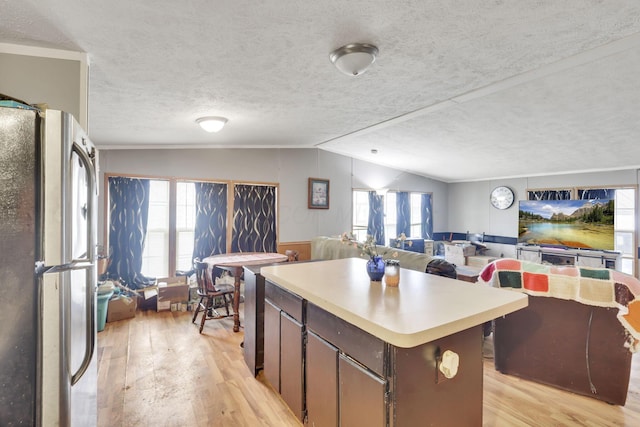 kitchen with light countertops, freestanding refrigerator, light wood-style floors, a kitchen island, and lofted ceiling