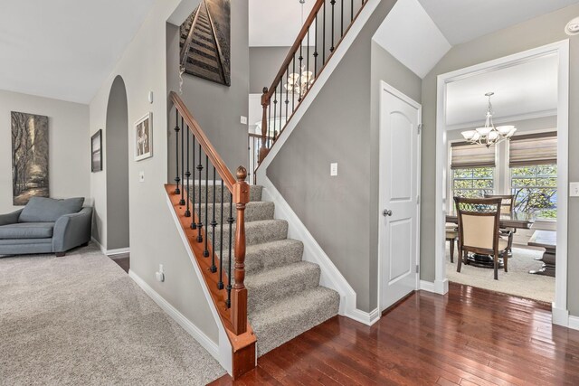 stairway featuring arched walkways, hardwood / wood-style flooring, baseboards, and an inviting chandelier
