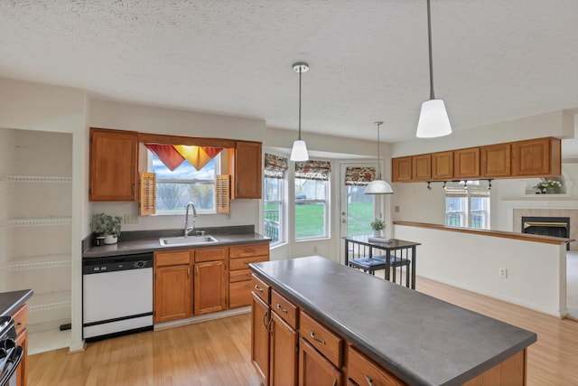 kitchen with light wood-style flooring, dark countertops, brown cabinetry, white dishwasher, and a sink